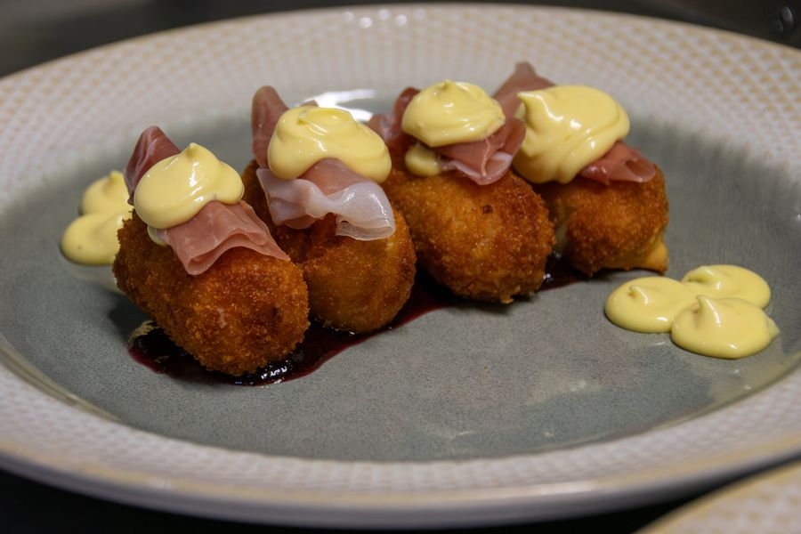 Manchego croquettes topped with prosciutto and aioli over red berry jam