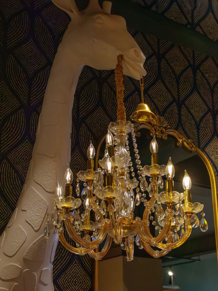 The sculpted white giraffe on patterned wallpaper beside a crystal chandelier at Restaurante Bocas