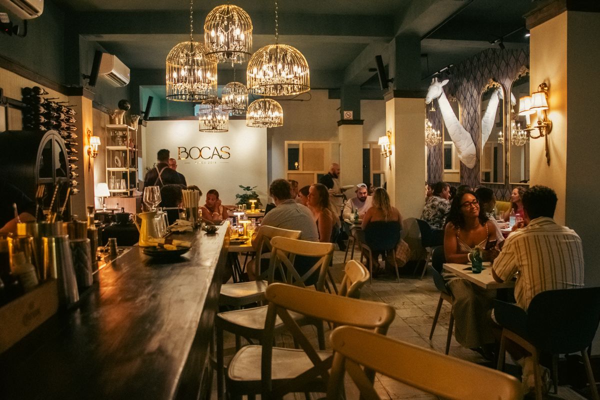The Restaurante Bocas dining room at night, full of guests under birdcage and crystal chandeliers